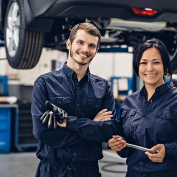 Two happy mechanics - man and woman standing by the car
