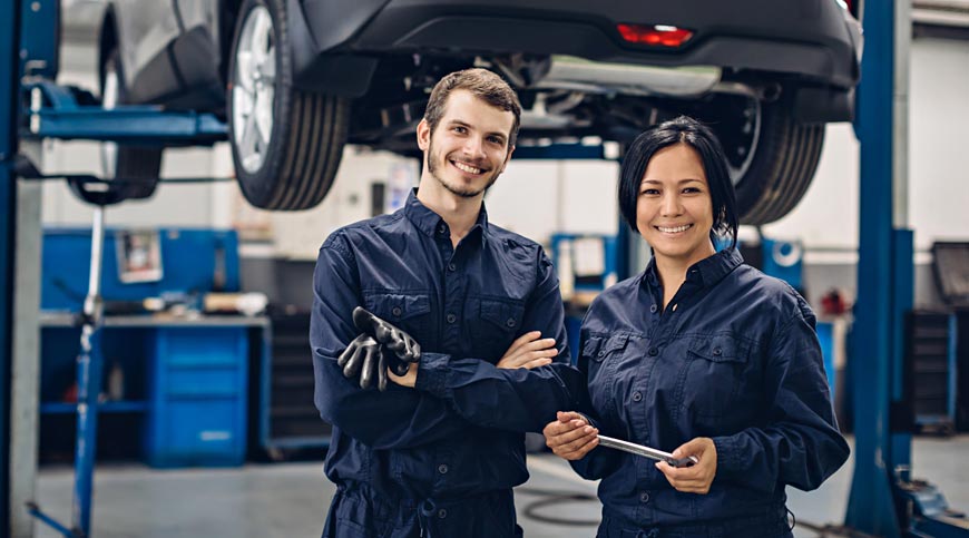 Two happy mechanics - man and woman standing by the car